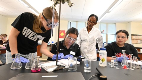 Students working in the chemistry lab with a professor observing.