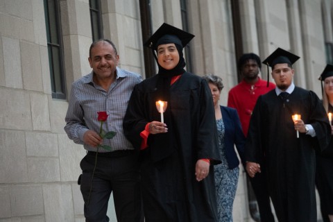 Graduate with cnadles and clasmates with roses