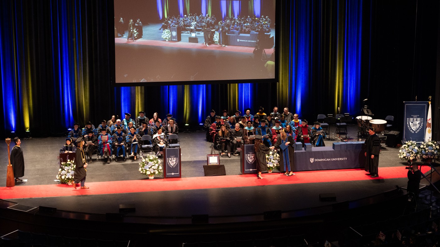 Graduates walk across the Rosemont Theatre stage to receive their diplomas from President Glena G. Temple at Dominican University's Spring Commencement Ceremony