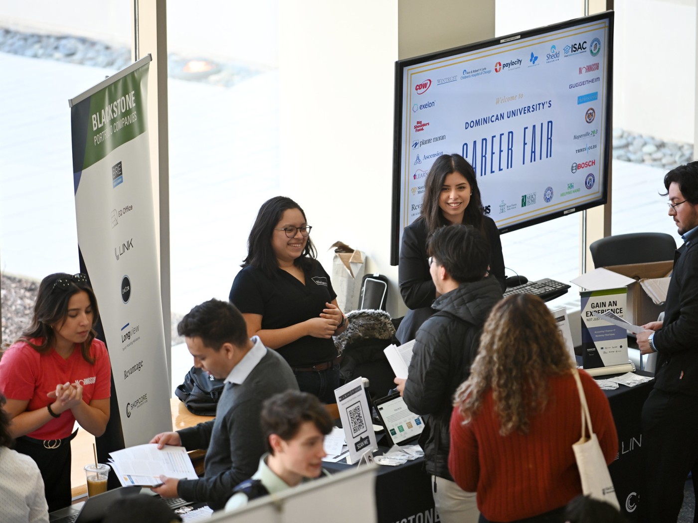 A group of female and male students shown standing around tables at Dominican University's Career Fair.