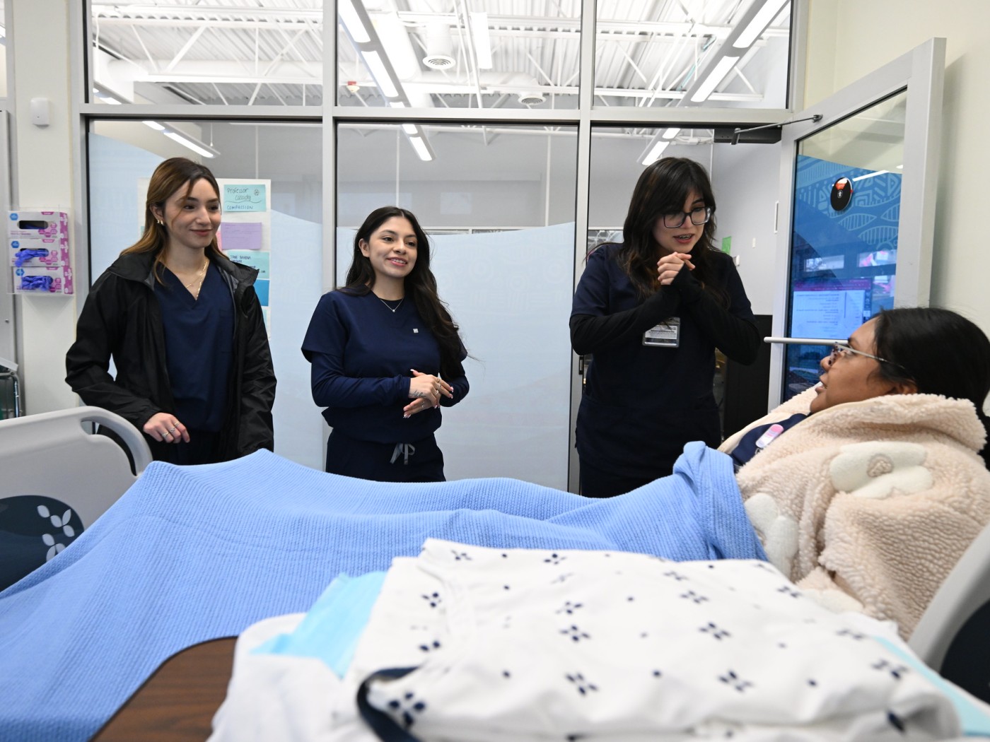 Three students observing patient in hospital bed